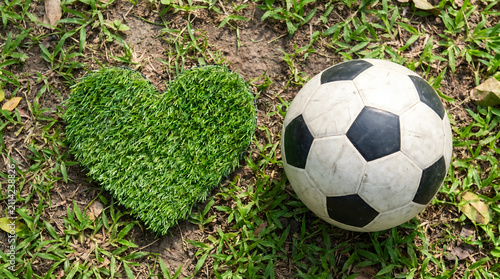 Classic soccer ball next to a green heart shaped turf on natural grass field background
