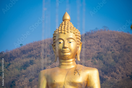 Golden Buddha Statue: A serene golden Buddha statue stands tall against a clear blue sky, with a gently sloping, dry hillside in the background. The statue exudes a sense of peace and spirituality.