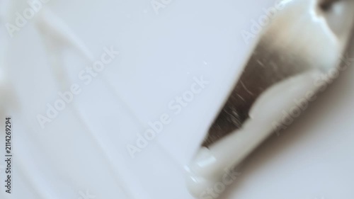Metal spatula spreading white cosmetic cream in smooth, wavy texture macro shot