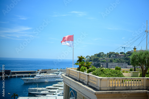 Monaco national flag waving above a luxury marina overlooking the Mediterranean Sea.
