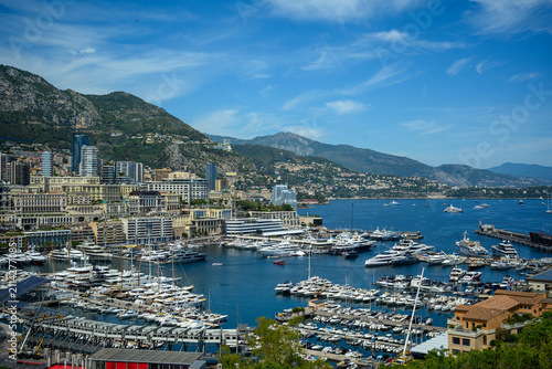 Panoramic view of Port Hercule in Monaco, showcasing luxury yachts, the Monte Carlo skyline, and the Mediterranean coastline surrounded by scenic mountains.