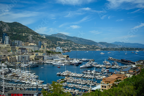 Panoramic view of Port Hercule in Monaco, showcasing luxury yachts, the Monte Carlo skyline, and the Mediterranean coastline surrounded by scenic mountains.