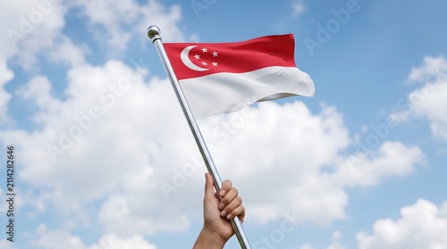 Hand holding waving Singapore national flag on metal pole against blue sky with white clouds