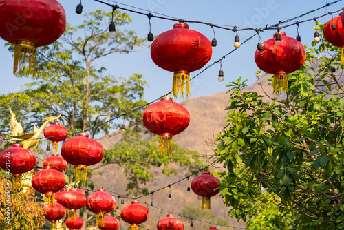 Red Lanterns Decorating Outdoors: A vibrant display of traditional red lanterns hanging from strings, illuminating an outdoor area with lush greenery and distant mountains.