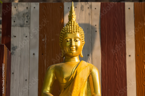 Golden Buddha Statue: A serene golden Buddha statue, adorned in saffron robes, radiates peace and enlightenment against a backdrop of striped wooden panels.
