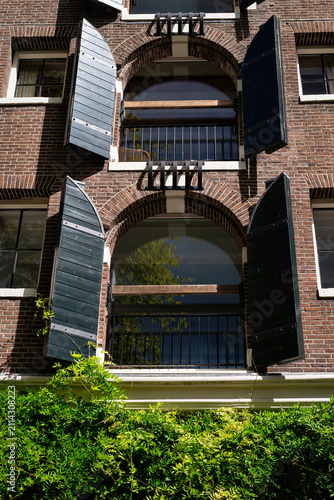 Historic brick building with arched windows and black shutters covered in greenery