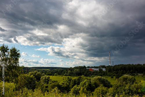 Obraz na płótnie Dramatic storm clouds gathering above a lush green forest landscape with a dista