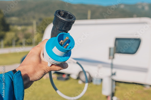 Φωτογραφία Hand holding electric hookup plug at campsite with caravan in background