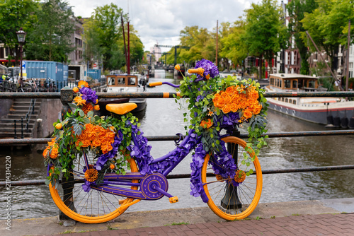 Decorated bicycle with colorful flowers on a bridge over an Amsterdam canal