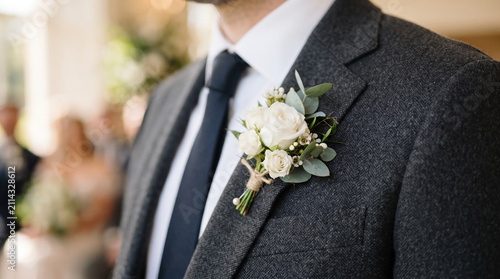 Man's elegant grey suit with white formal boutonniere on lapel, featuring delicate roses and eucalyptus foliage.