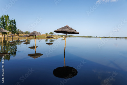 Quadro su tela Straw umbrellas standing in tranquil flooded alentejo alqueva lake