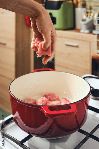 Cook adds meat to pot on stove in a kitchen setting during meal preparation session