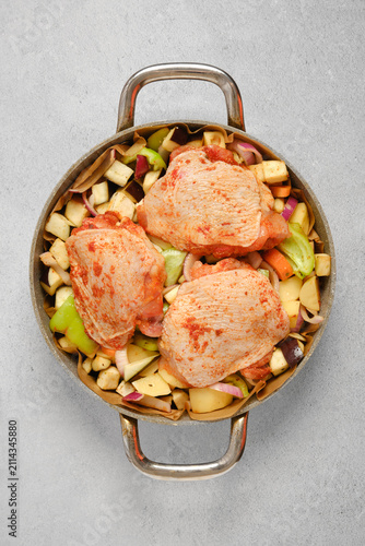 Marinated chicken thighs placed on vegetables before cooking in a pot