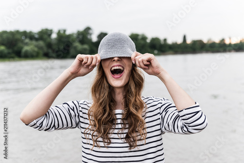 Laughing woman playing with wooly hat at a river