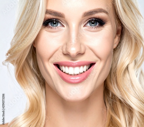 Close-up beauty portrait of a smiling blonde woman showing clean white teeth and bright expression.