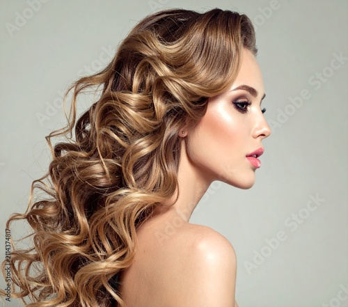 Side profile of a glamorous woman showing off voluminous brown wavy curls and soft professional makeup.