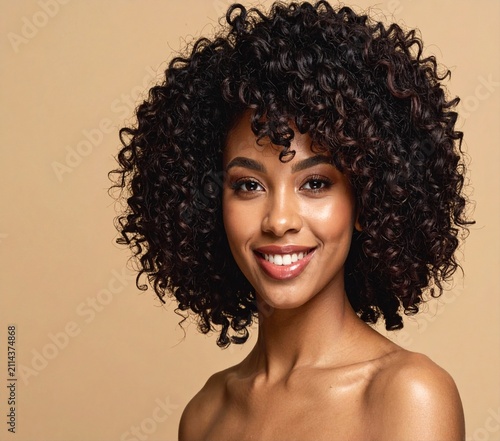 Portrait of a happy smiling Black woman with voluminous natural afro curly hair against a warm beige background.