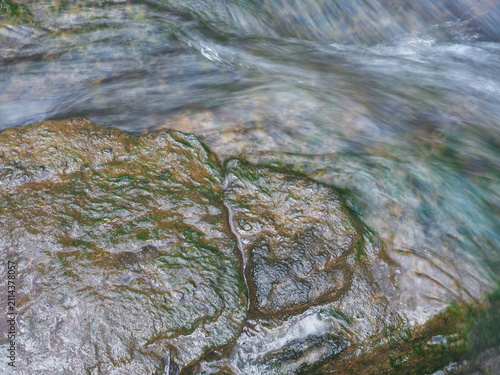 High-angle view of clean natural water flowing rapidly over dark, textured river stones and rocks covered in green moss. 