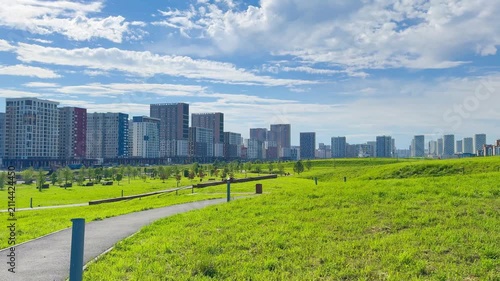 Urban landscape showcasing modern buildings and green park area with walking path under a clear blue sky in a vibrant city setting