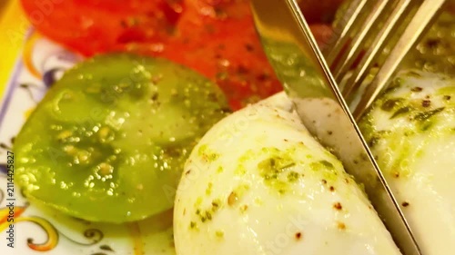 Close-up macro view of fresh burrata cheese being cut, revealing the creamy liquid center over green and red tomatoes. Italian food, caprese salad and gourmet appetizer concept