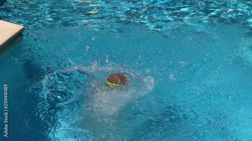 A young child wearing swim goggles splashes joyfully into the clear swimming pool. He swims happily in the sparkling blue water. The exciting moment brings pure fun and carefree energy.