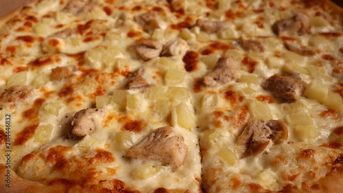 Freshly baked Hawaiian pizza with chicken and pineapple. The fluffy crust, topped with melted mozzarella cheese, reveals juicy pieces of chicken and diced fruit with a golden crust. 
