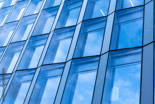 Across the angled surface, blue glass divides a building into windows, while reflection and geometry animate the facade and architecture of Oslo, Norway under daylight