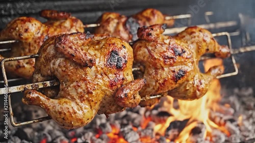 Whole chickens roasting on a rotisserie over hot charcoal