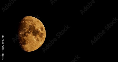 Detailed golden gibbous moon moving across black sky night time lapse