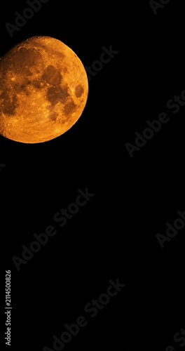 Vertical time lapse of massive orange moon setting behind tv tower silhouette at night