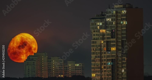 Massive orange full moon setting behind city skyscrapers at night time lapse
