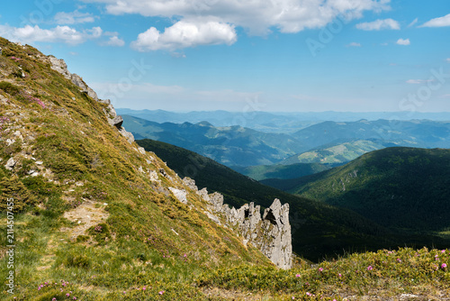 Obraz na plátně A horizontal high-angle shot of tall stone rock formations and rocky pillars on a steep grassy mountainside overlooking a deep green valley, ideal for geology and adventure travel marketing