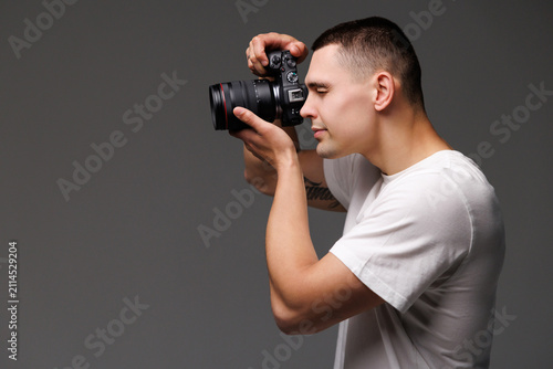 Young male photographer with camera in professionally equipped on gray background