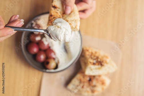 Fotografie A hand lifts a piece of warm, crispy bread, ready to scoop into a rich, creamy dip, surrounded by succulent grapes