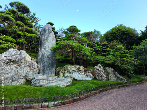 The traditional Chinese green garden landscape features manicured trees and volcanic rock formations at nightfall