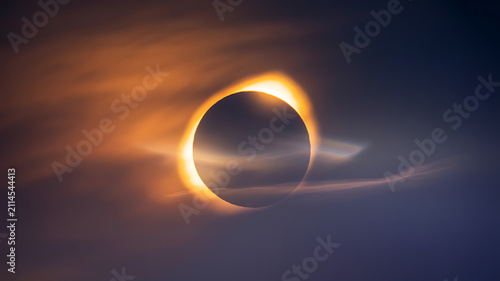 Total solar eclipse with a glowing sun corona ring shining through soft clouds in the dark evening sky during a rare astronomical event in space capturing the beauty of the universe