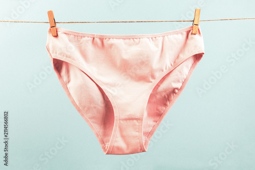 washed pink women's panties made of cotton with clothespins hanging on a rope on a blue background, photos in pale pastel colors