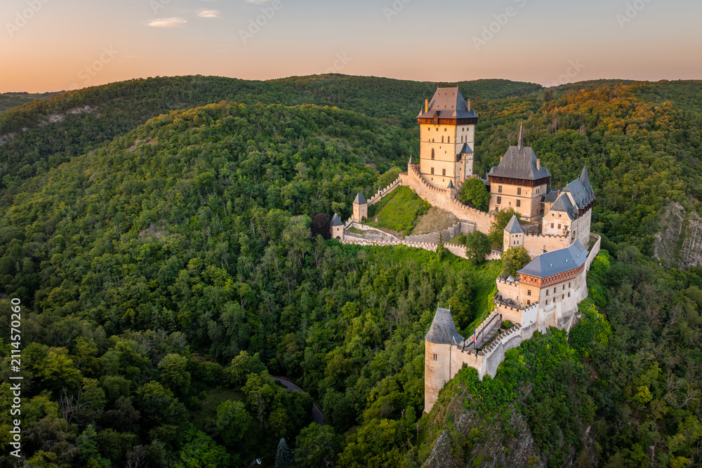 Obraz premium Aerial view of iconic gothic royal Karlstejn Castle surrounded by lush green forests at golden hour sunset, UNESCO candidate site, Central Bohemia, Czech Republic ( Hrad Karlštejn-Česká Republika )
