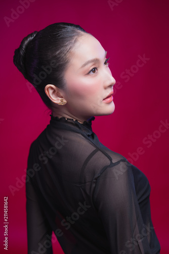 Foto A striking woman with slicked-back hair stares directly into the lens with quiet intensity, radiating self-possessed elegance and effortless glamour against a deep crimson studio backdrop