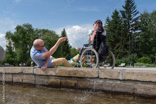 Foto husband plays jokes with a paralyzed female disabled man in a wheelchair on a wa