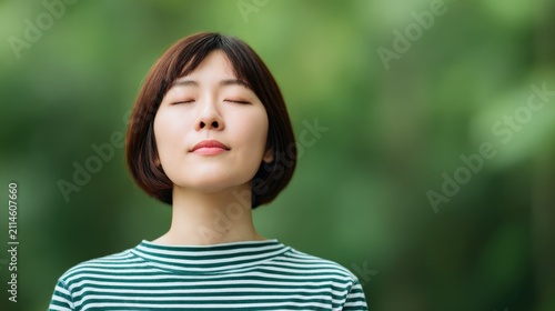 Young woman with short brown hair standing outdoors with eyes closed enjoying fresh air peaceful moment in nature