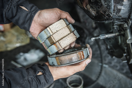 Hands of mechanic inspecting motorbike brake pads in garage