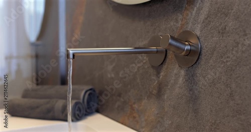 Wall mounted faucet with flowing water on a natural stone surface, static video highlights the sleek built in fixture in a luxury modern bathroom where refined materials and soft daylight create