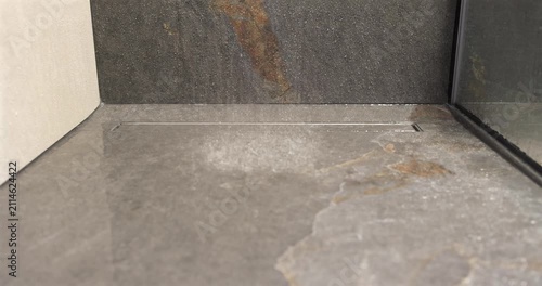 Stone shower floor with built in drain under falling water, static slow motion footage isolates the first impact of descending drops and delicate spray across the textured surface