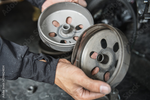 Mechanic hands holding scooter clutch bell and outer housing for inspection and maintenance in motorcycle workshop