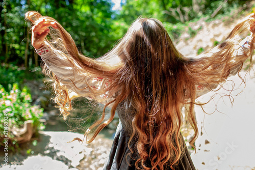 Young Ukrainian woman in embroidered clothing showing her long natural hair in a sunlit forest, combining feminine beauty, cultural tradition and nature.