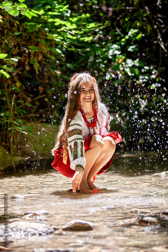 Young Ukrainian woman in embroidered traditional clothing sitting beside a clear forest stream, expressing serenity, cultural identity and connection with nature.