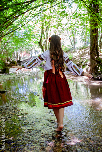 Young Ukrainian woman in embroidered traditional clothing sitting beside a clear forest stream, expressing serenity, cultural identity and connection with nature.