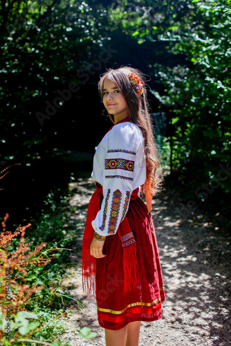 Young Ukrainian woman in a traditional embroidered costume standing in a green forest, combining cultural heritage, femininity and a close connection with nature.