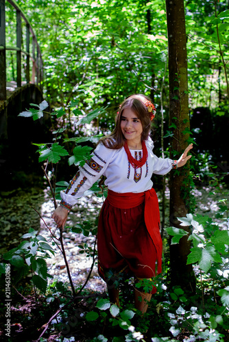 Young Ukrainian woman in a traditional embroidered costume standing in a green forest, combining cultural heritage, femininity and a close connection with nature.